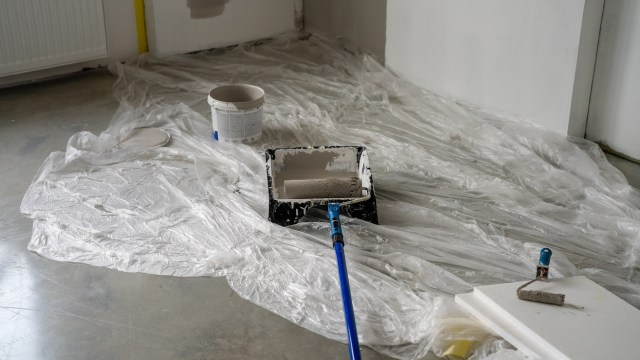 A paint roller and tray sit on a sheet of plastic in a room undergoing painting.
