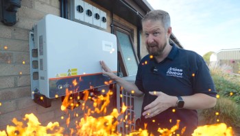 A man points to a solar inverter mounted on a brick wall with a graphic of orange flames in the foreground.