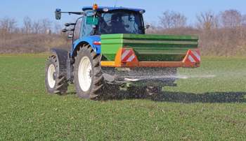 A tractor spreading fertilizer across a lush green field.