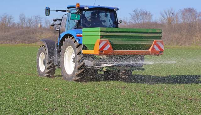 A tractor spreading fertilizer across a lush green field.