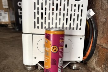 A can of passion fruit drink is placed in front of a white appliance with ventilation holes.