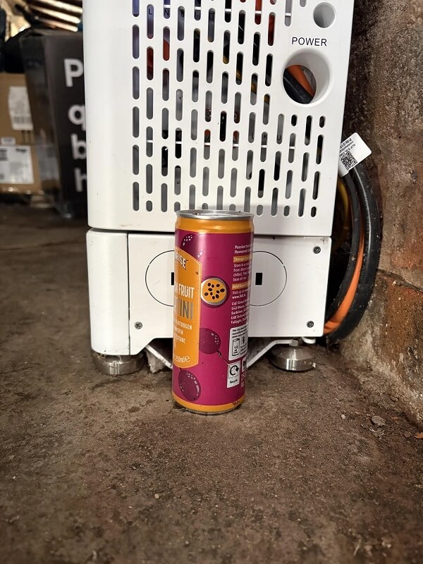 A can of passion fruit drink is placed in front of a white appliance with ventilation holes.