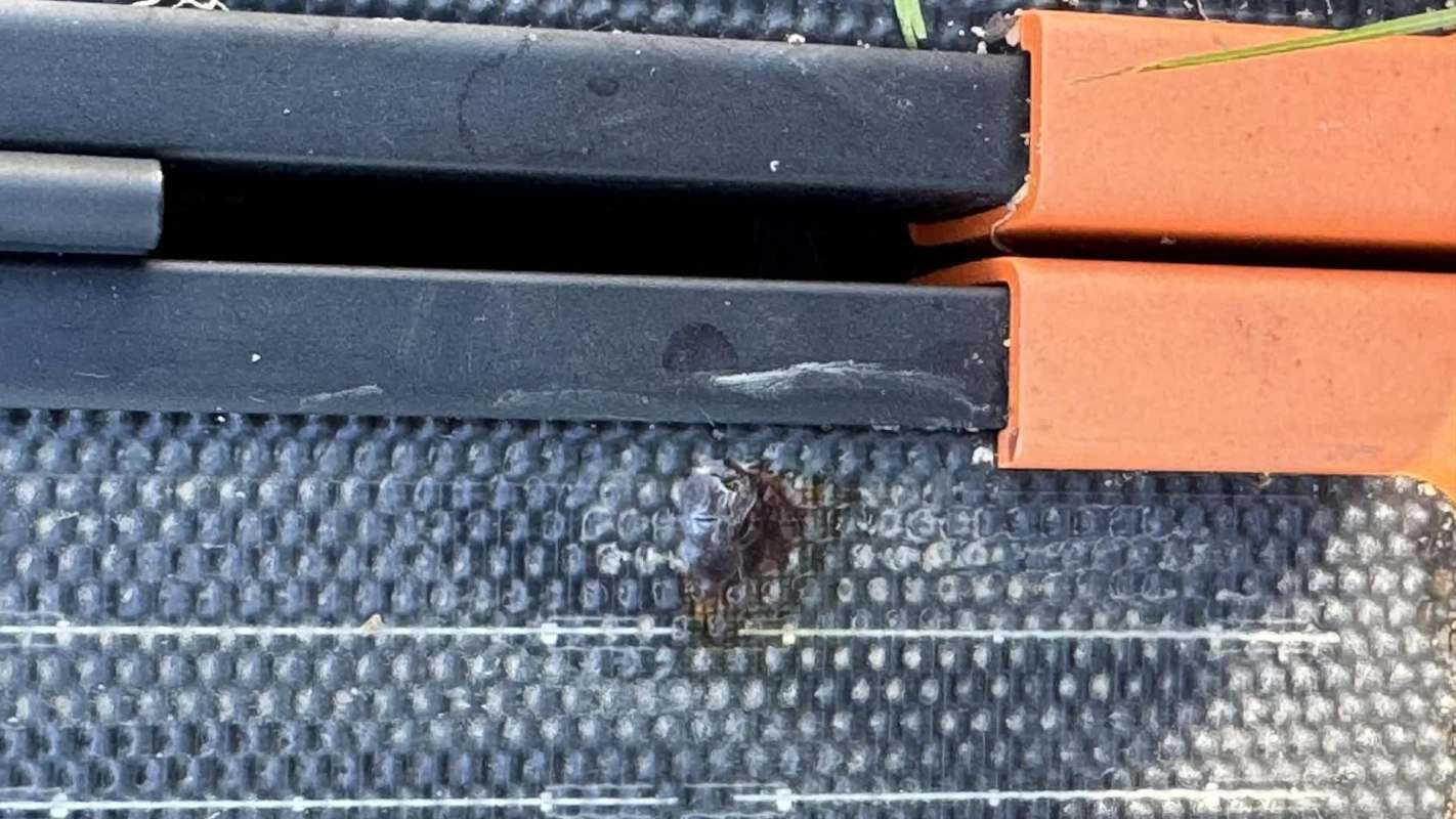 A black solar panel with orange clamps and a small rip on the surface.