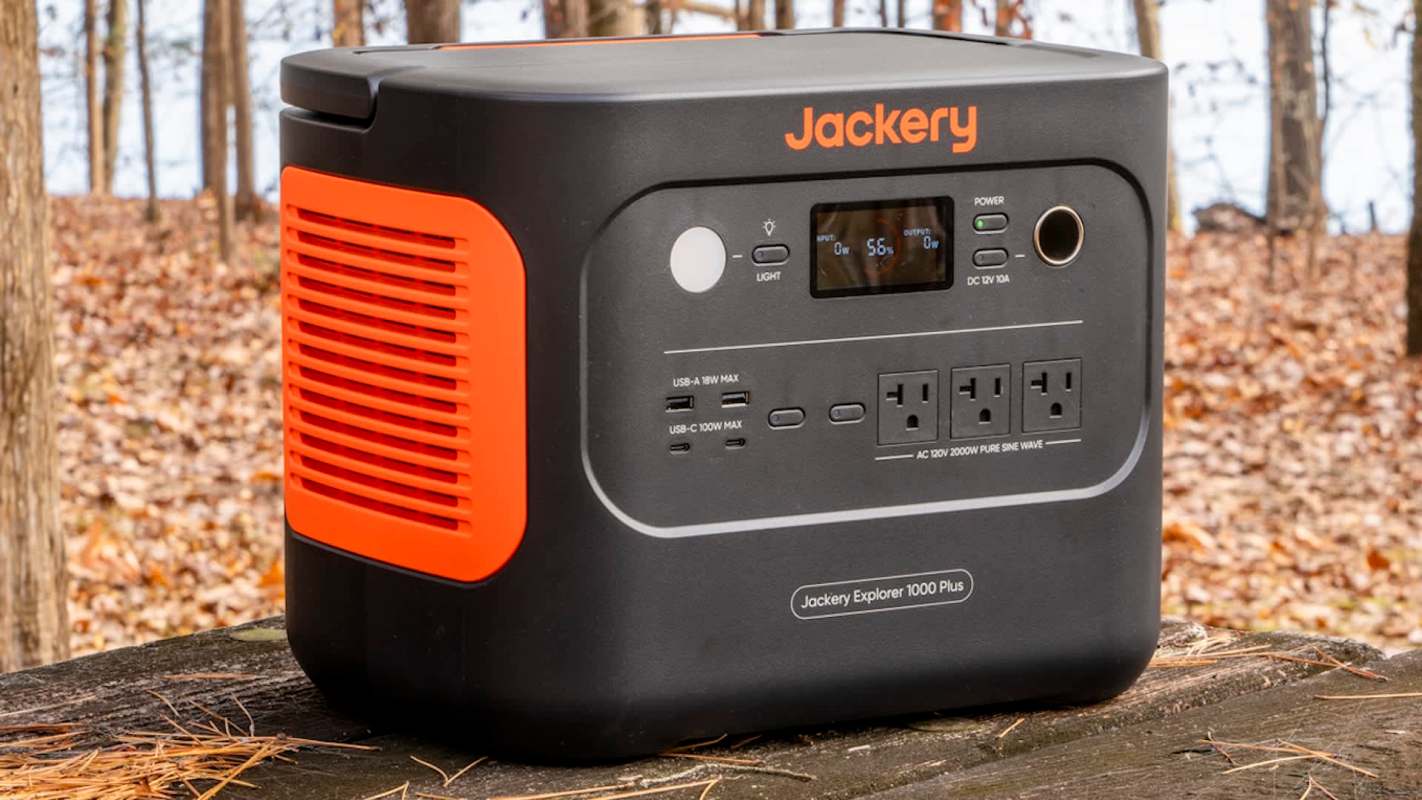 A Jackery Explorer 1000 Plus portable power station on a wooden surface in a wooded area.