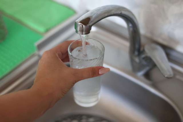 A hand holding a glass while water is being poured from a faucet.