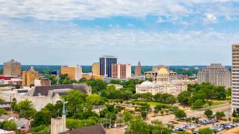 A skyline of Jackson, Mississippi, featuring high-rise buildings, green parks, and a prominent dome-shaped structure.