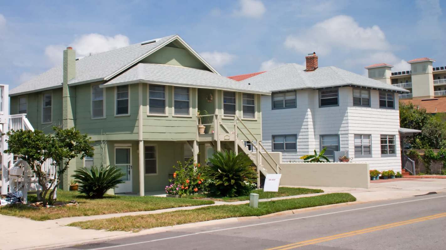 Two residential houses, one green and one white, with steps and plants in the yard.