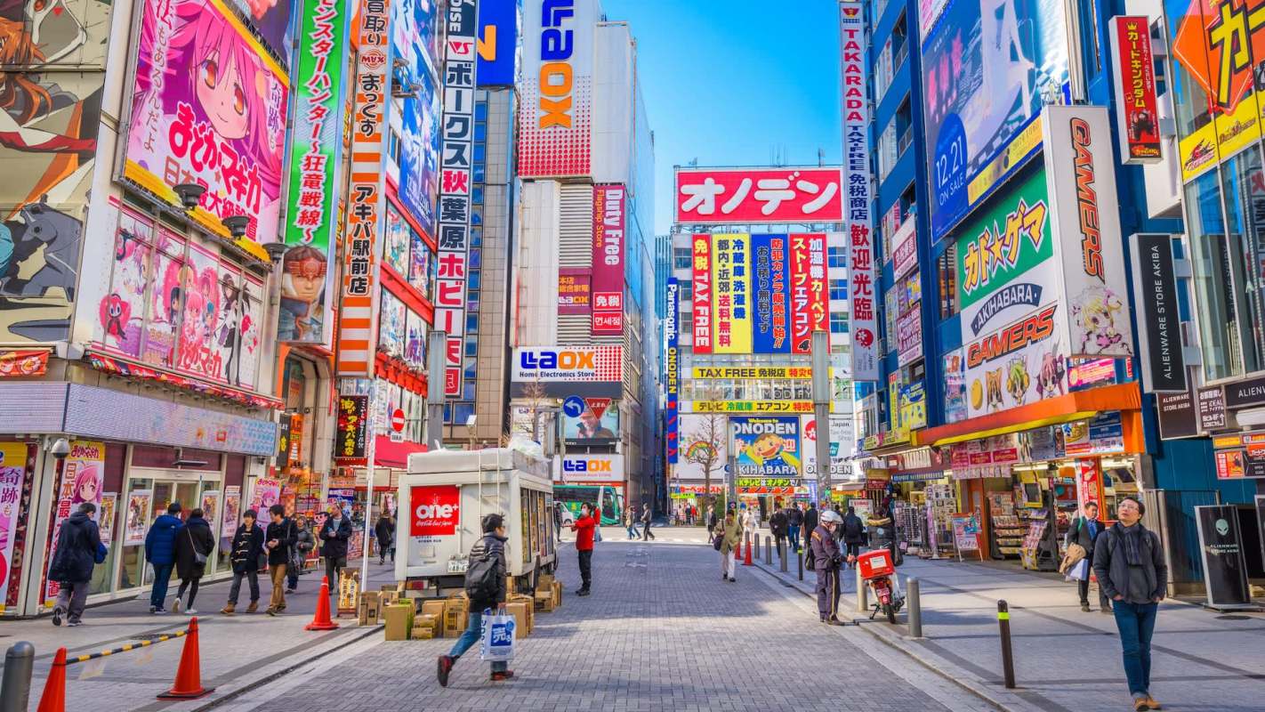 A busy street in Akihabara, Tokyo, lined with colorful advertisements and people walking.