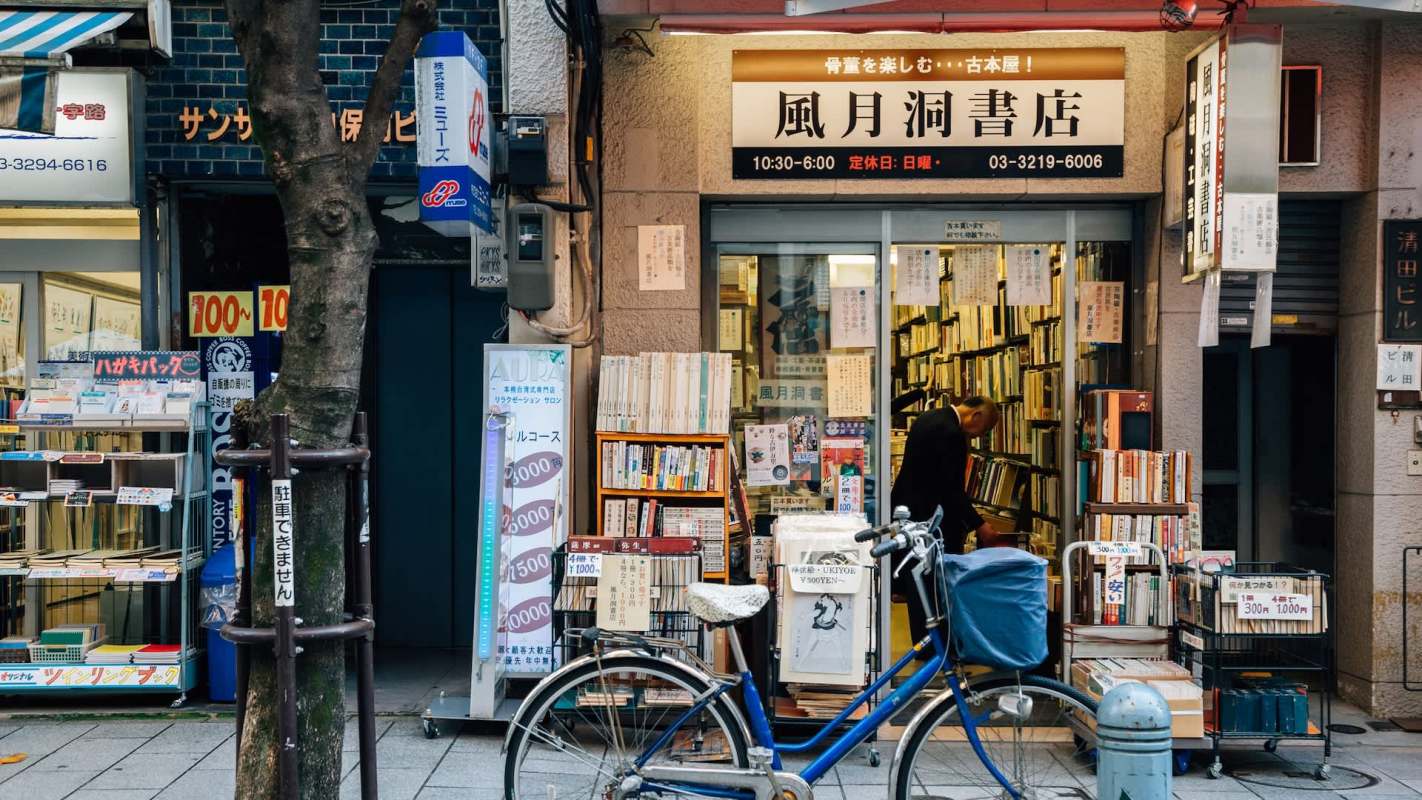 An exterior of a Japanese bookstore with shelves of books and a blue bicycle parked outside.