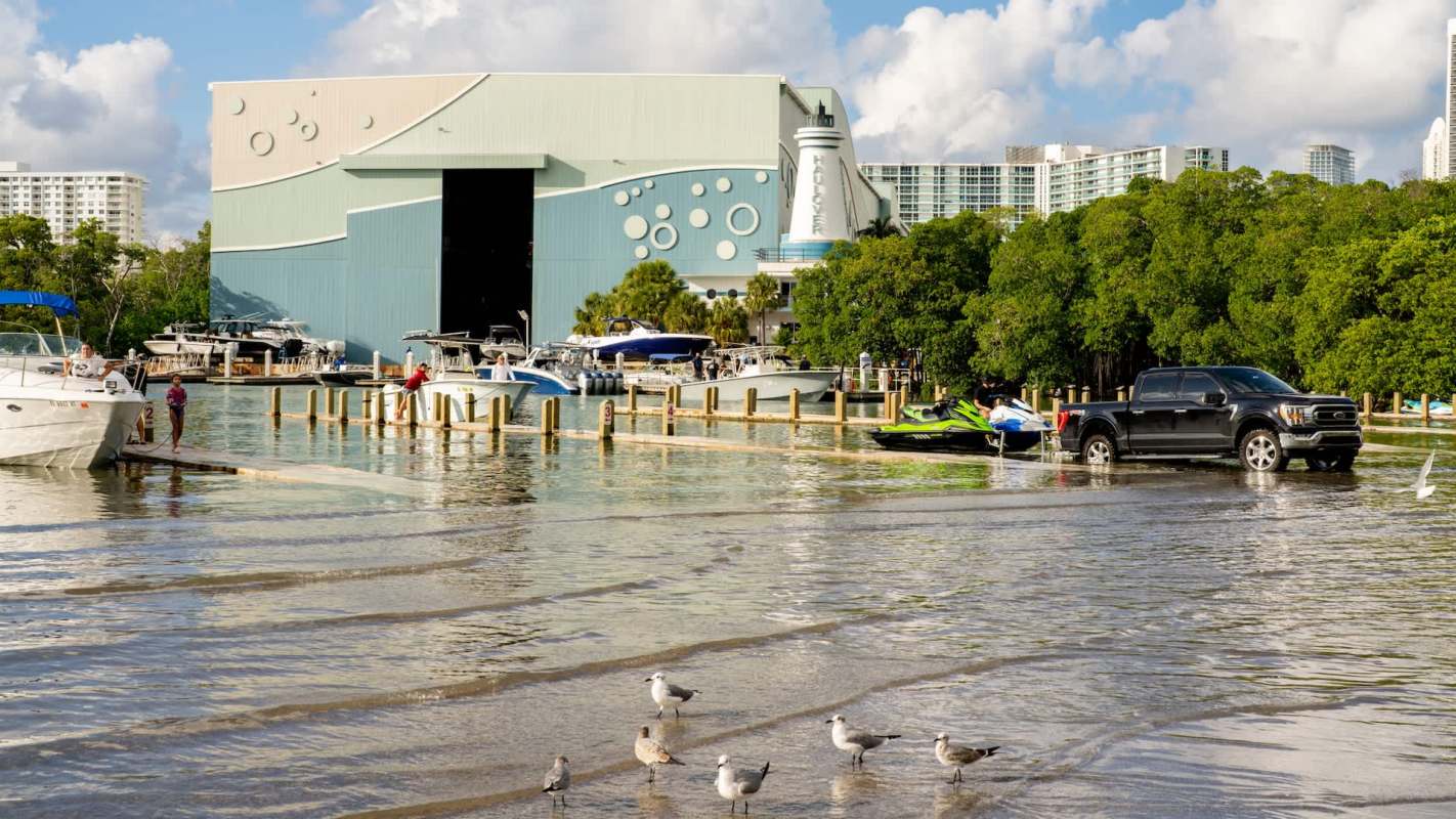 A marina scene with boats, a jet ski, and people near a storage building by flood waters.