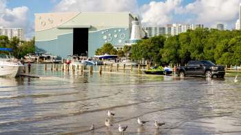 A marina scene with boats, a jet ski, and people near a storage building by flood waters.