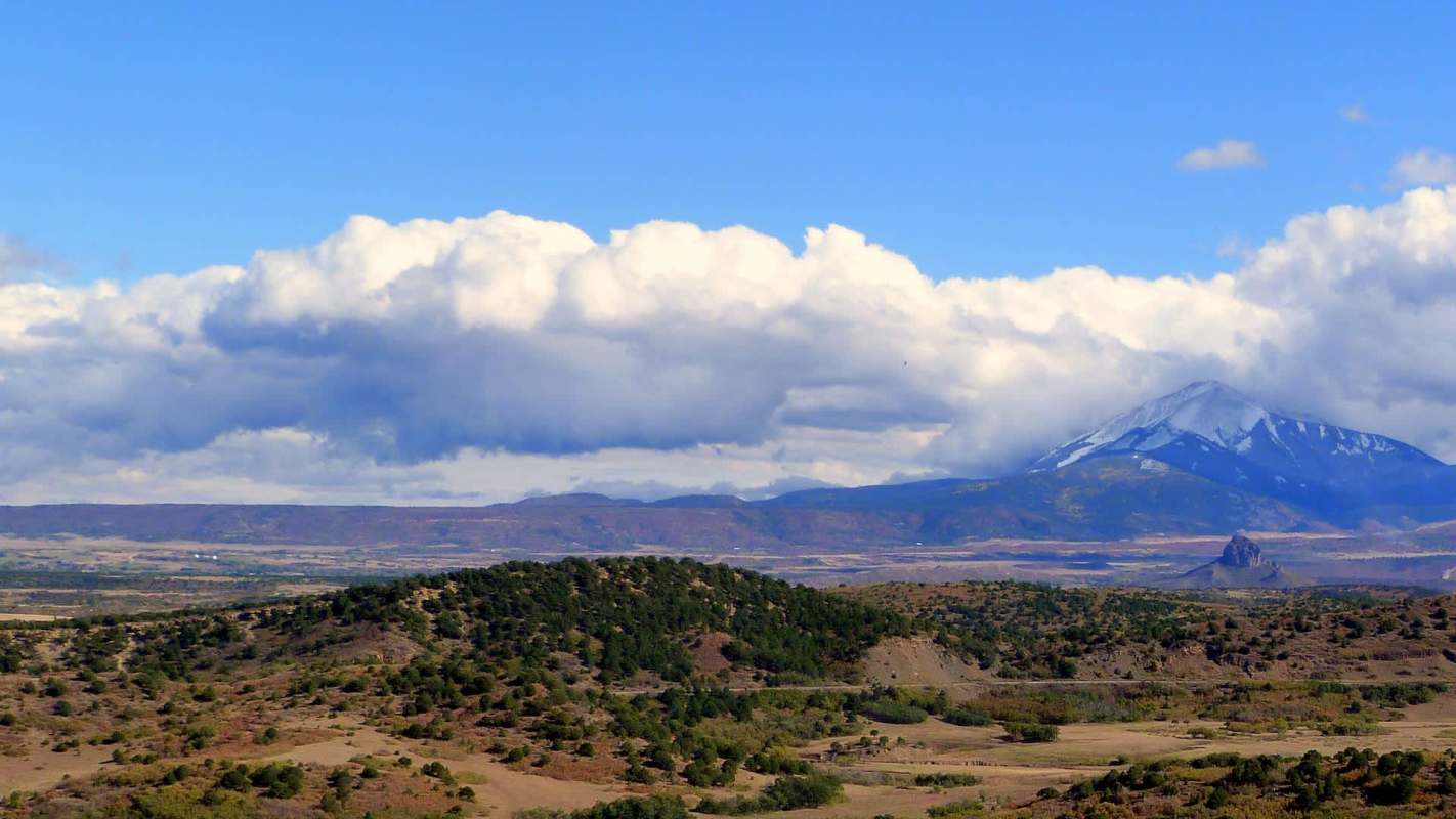 A mountainous landscape with rolling hills, green vegetation, and a partly cloudy sky.