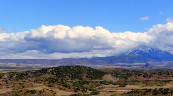 A mountainous landscape with rolling hills, green vegetation, and a partly cloudy sky.