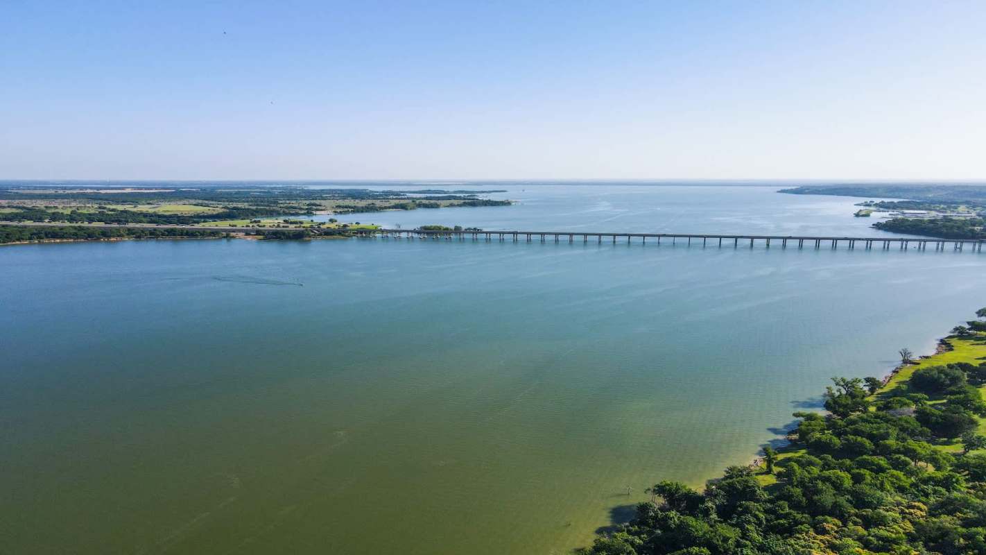 A wide river with a bridge crossing over, surrounded by green vegetation and open land.