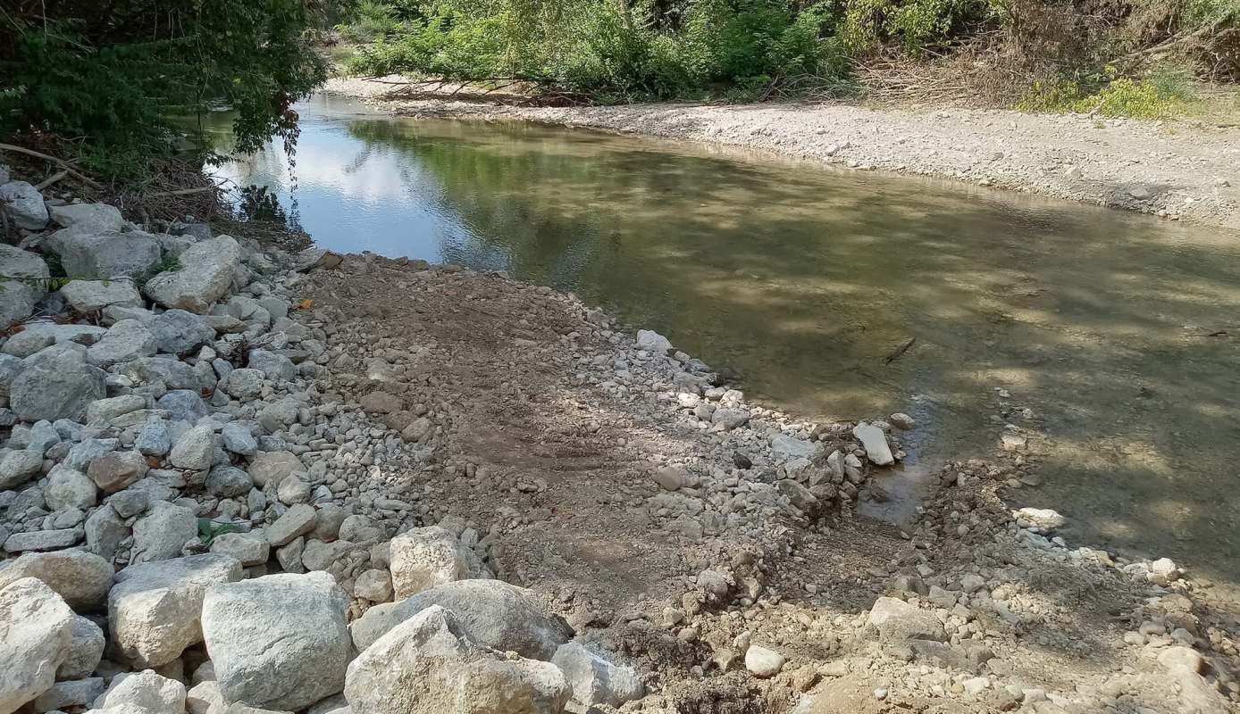 A rocky bank along a shallow river surrounded by greenery.
