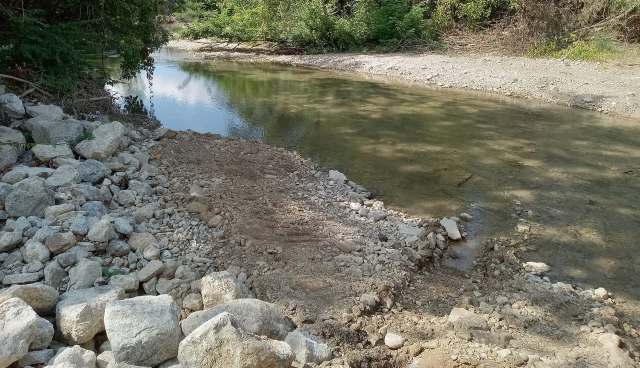 A rocky bank along a shallow river surrounded by greenery.