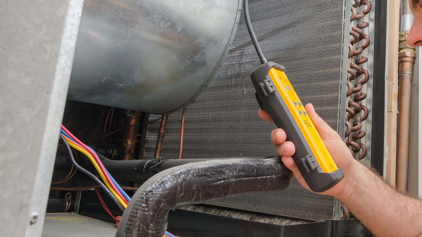 A person using a testing device on an HVAC unit with exposed wiring and copper tubing.
