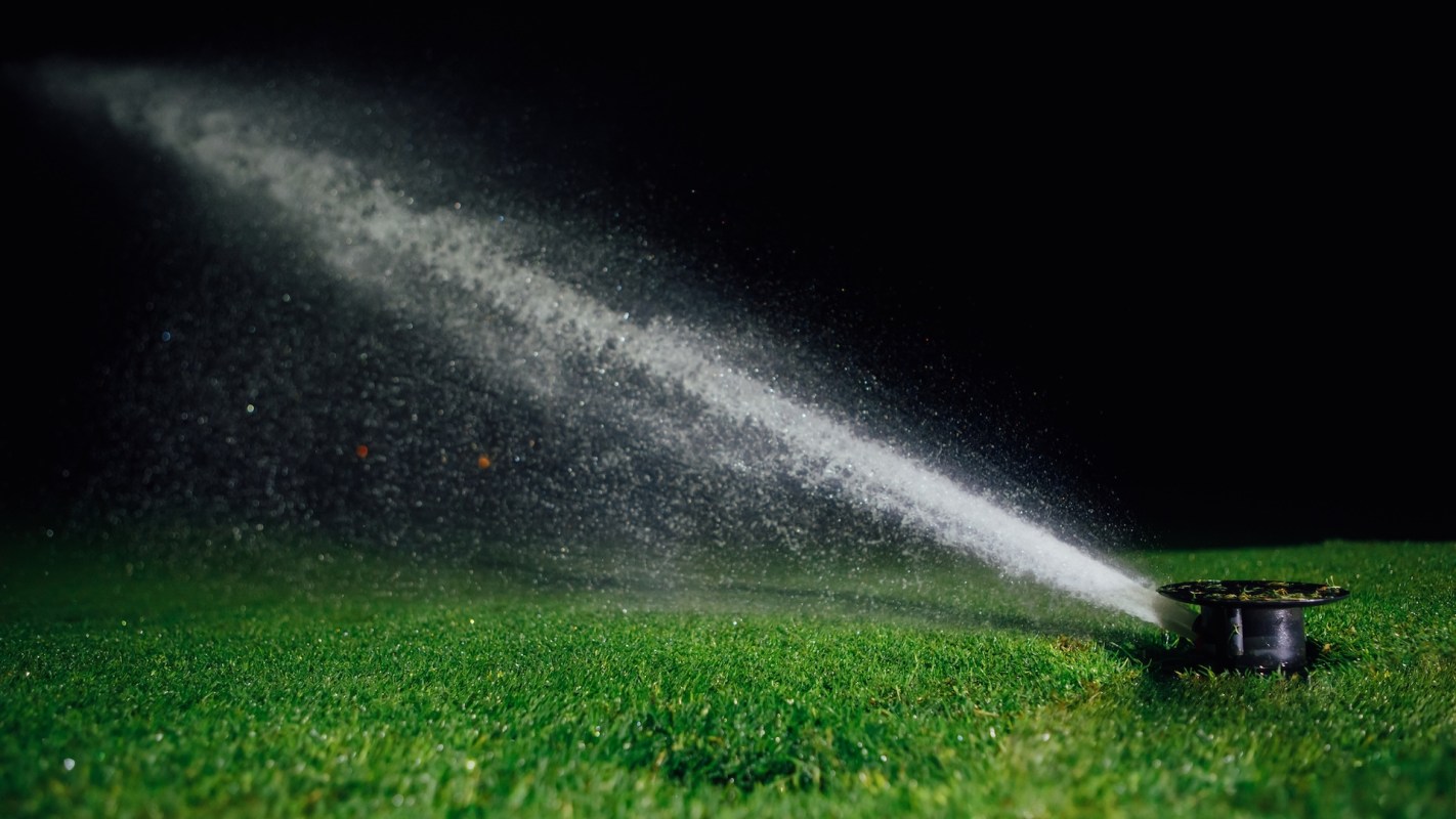 A sprinkler sprays water over a patch of grass at night.