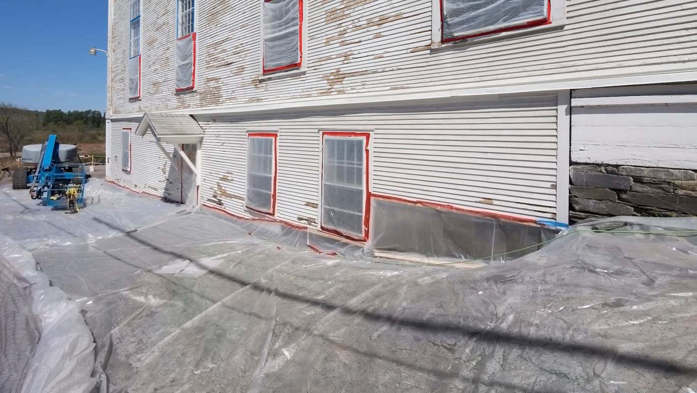 A building undergoing restoration, with plastic sheeting and equipment positioned nearby.