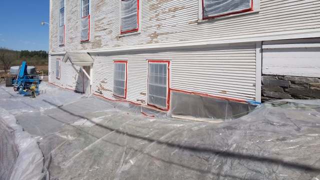 A building undergoing restoration, with plastic sheeting and equipment positioned nearby.