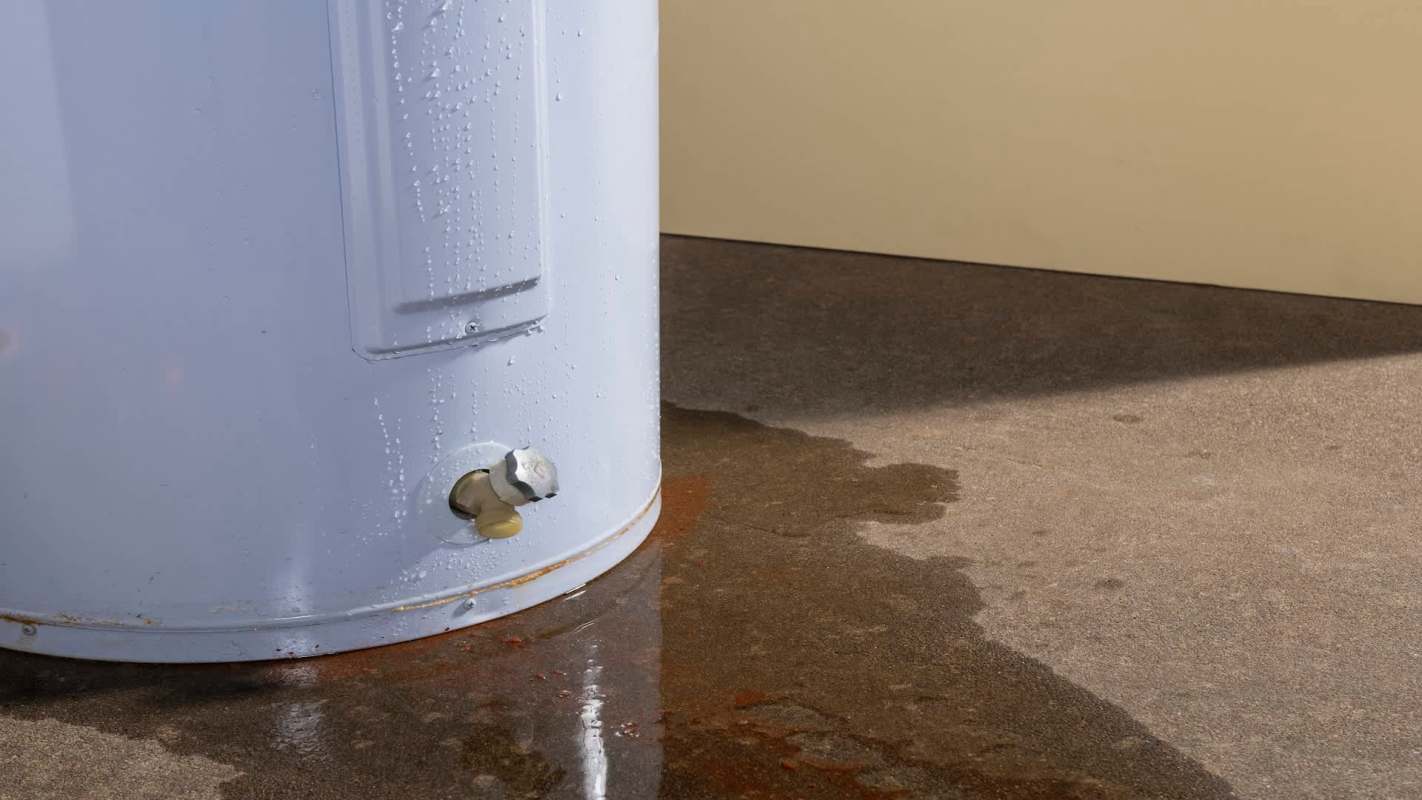 A water heater with condensation and a puddle of water on the ground.