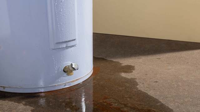 A water heater with condensation and a puddle of water on the ground.