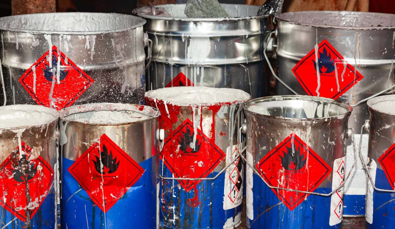 Several metal buckets with warning labels and splattered paint in various colors.