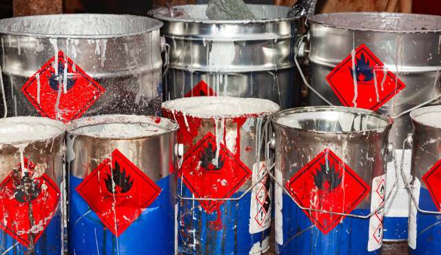 Several metal buckets with warning labels and splattered paint in various colors.