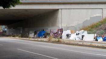 A collection of makeshift shelters and displaced items under a highway overpass.