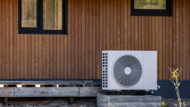 An outdoor air conditioning unit beside a wooden wall and a window.