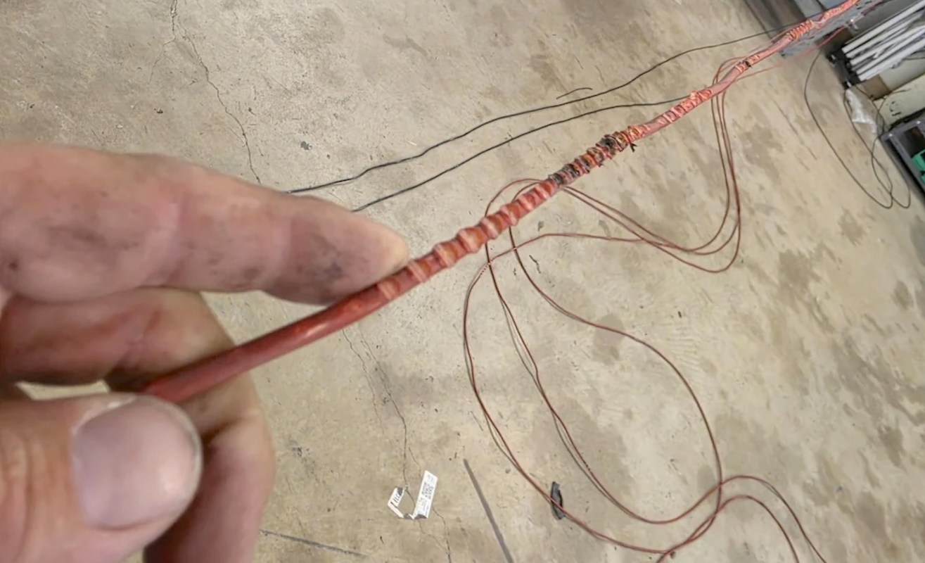 A hand holds a red wire with distinct twists, surrounded by other tangled wires on a concrete surface.