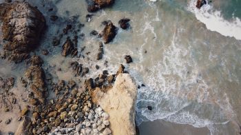 A rocky shore meets the ocean, with waves lapping at the sand and stones.