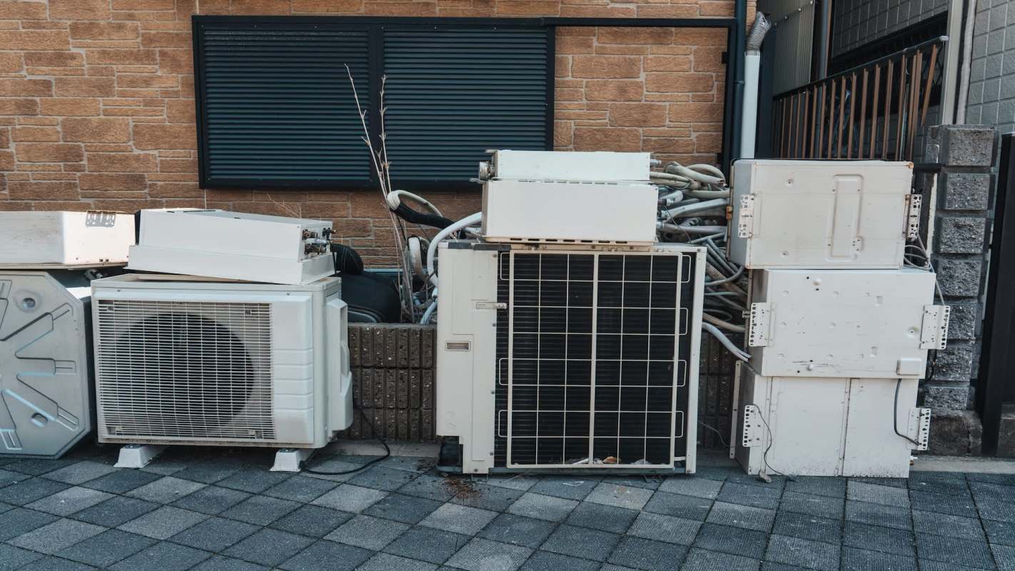Several discarded air conditioning units and equipment against a brick wall.
