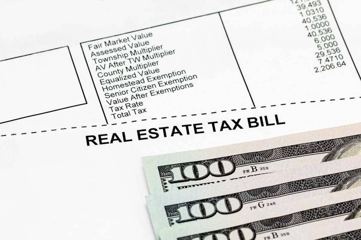 A real estate tax bill with listed values and several hundred dollar bills in the foreground.