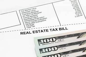A real estate tax bill with listed values and several hundred dollar bills in the foreground.