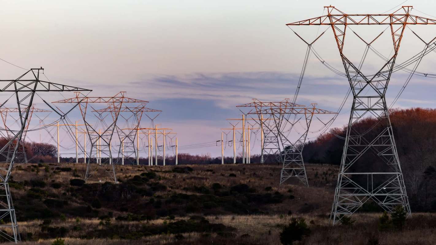 Power lines stretch across a grassy landscape under a twilight sky.