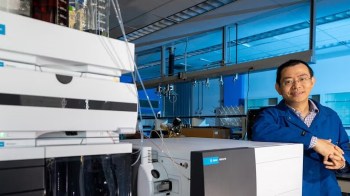 A scientist stands next to laboratory equipment in a lab setting.