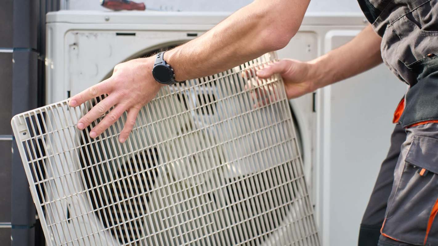 A person removes a grille from an outdoor air conditioning unit.