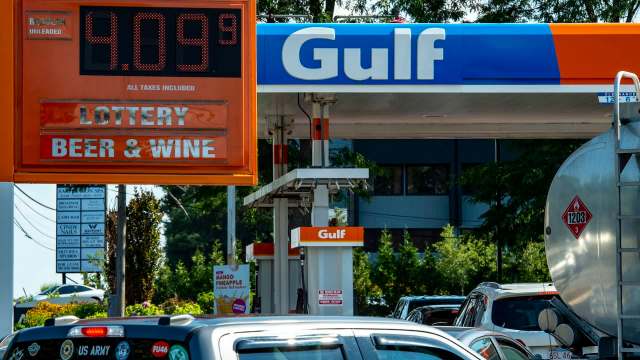 A gas station sign displays fuel prices and advertisements for lottery, beer, and wine.