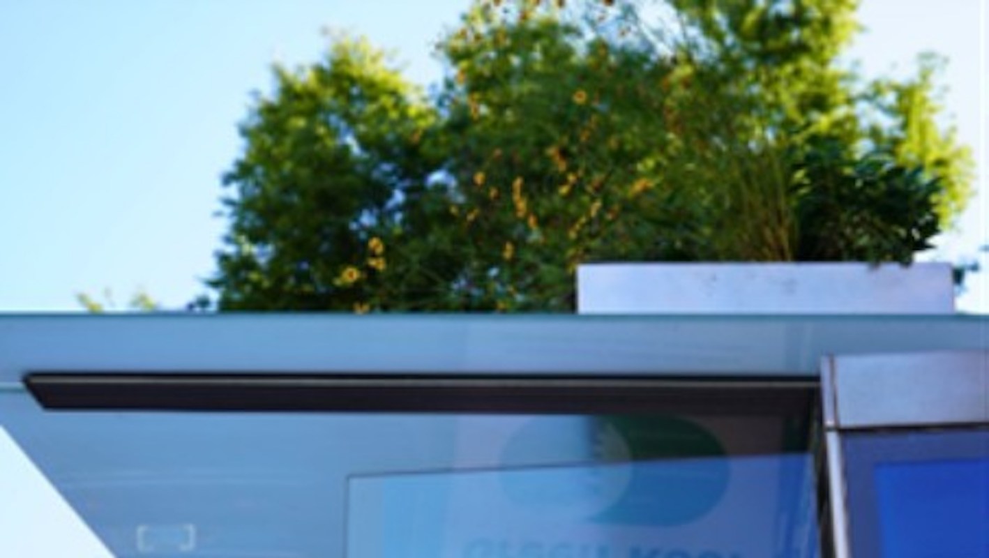 A bus stop with glass and greenery on the roof against a clear blue sky.