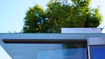 A bus stop with glass and greenery on the roof against a clear blue sky.