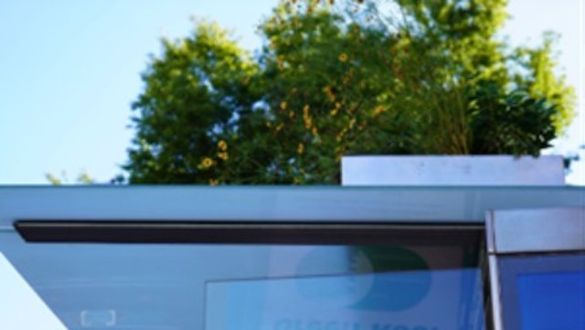 A bus stop with glass and greenery on the roof against a clear blue sky.