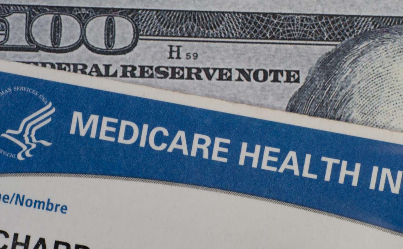 A Medicare card partially covering a hundred dollar bill.