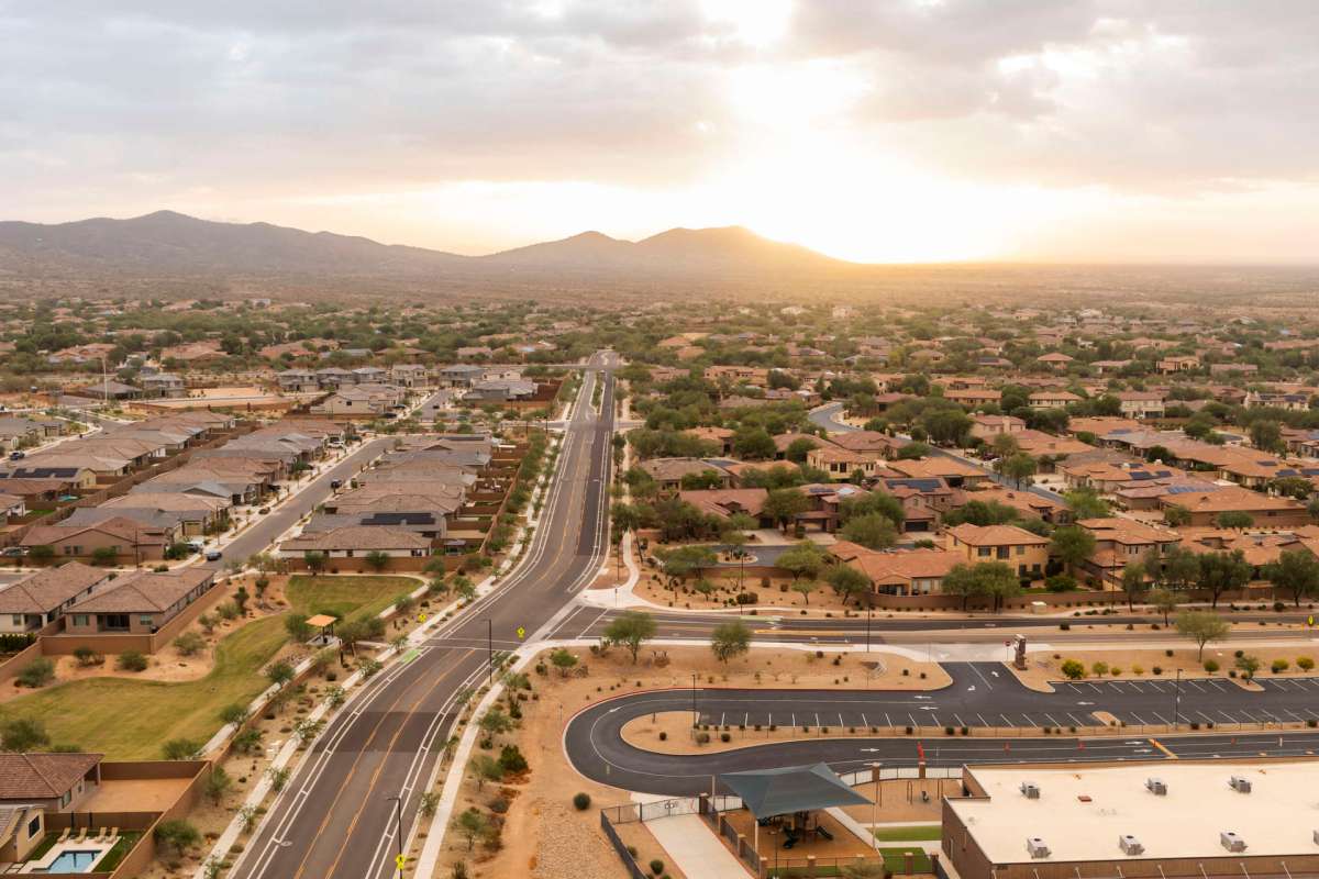 Aerial view of a residential area with houses, roads, and mountains in the background at sunset.