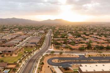 Aerial view of a residential area with houses, roads, and mountains in the background at sunset.