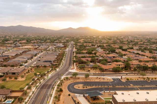 Aerial view of a residential area with houses, roads, and mountains in the background at sunset.