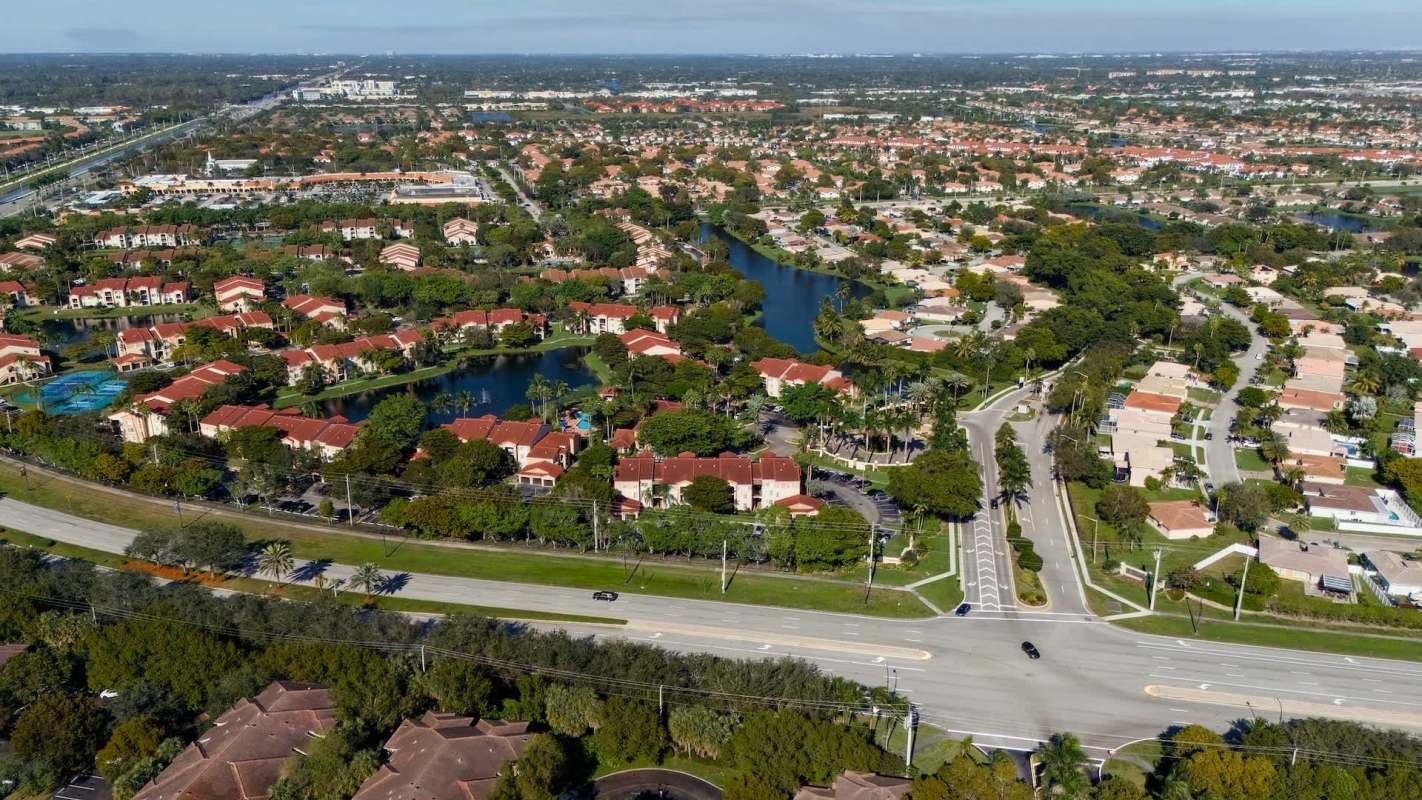 An aerial view of a suburban neighborhood with houses, a winding road, and a small pond.