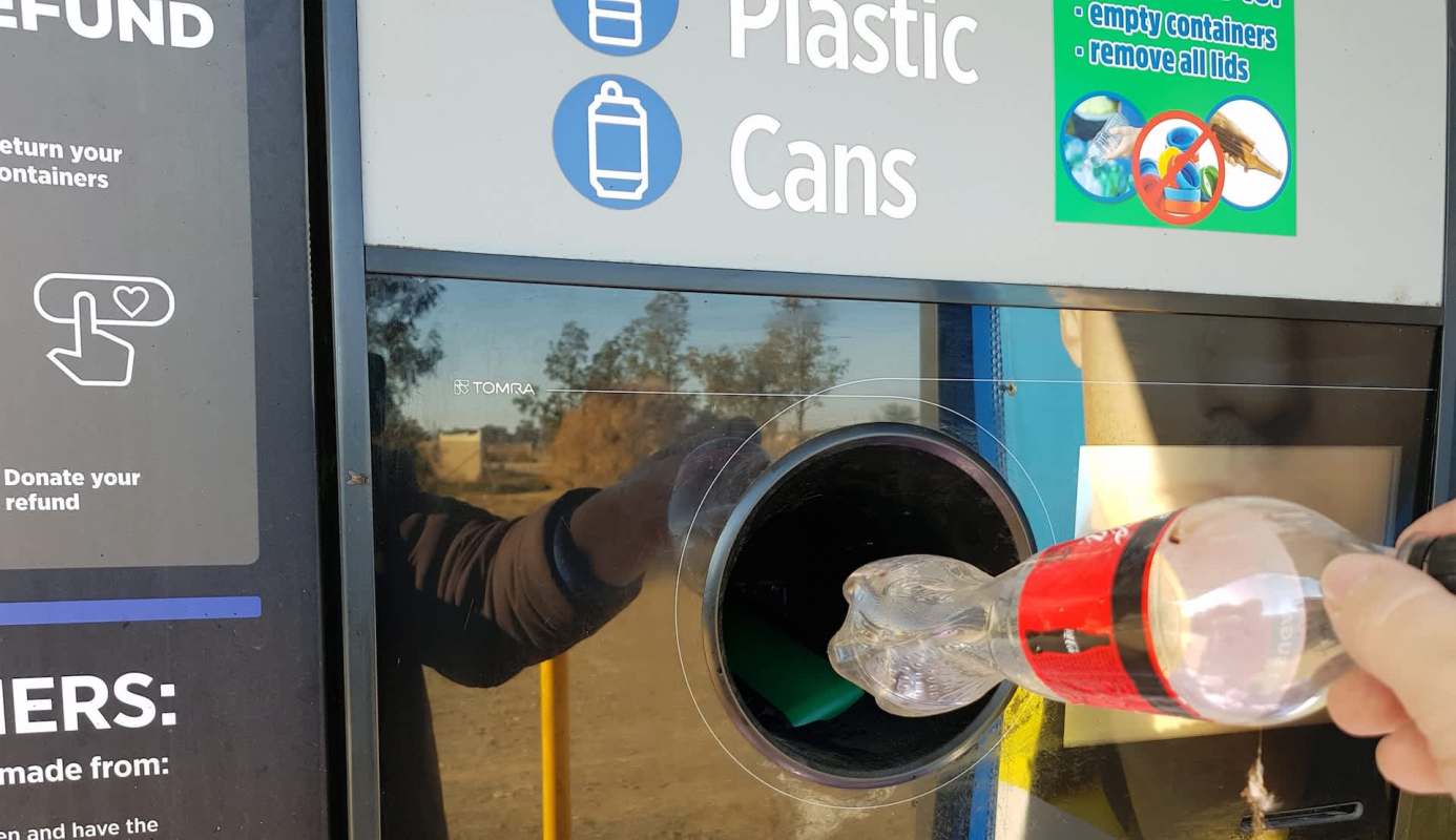 A person deposits a plastic bottle into a recycling machine with instructions nearby.