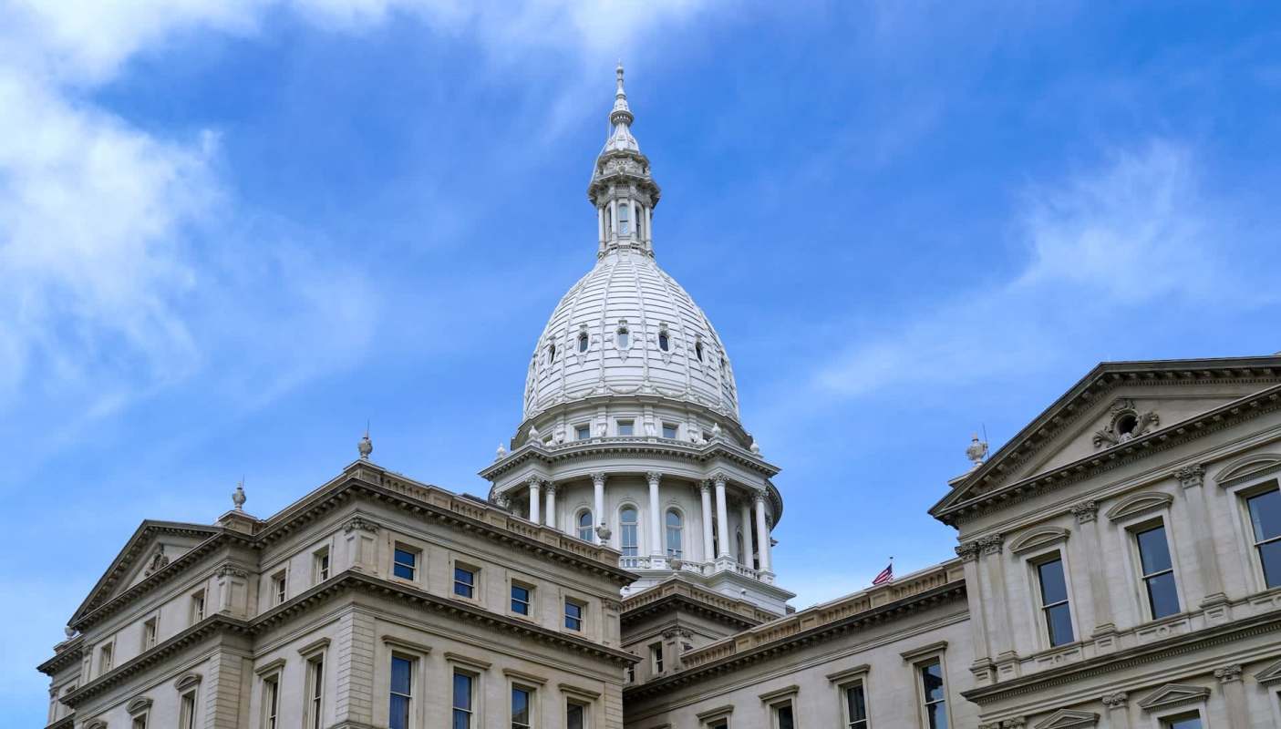 The dome of a historic building rises above surrounding architecture under a blue sky with clouds.