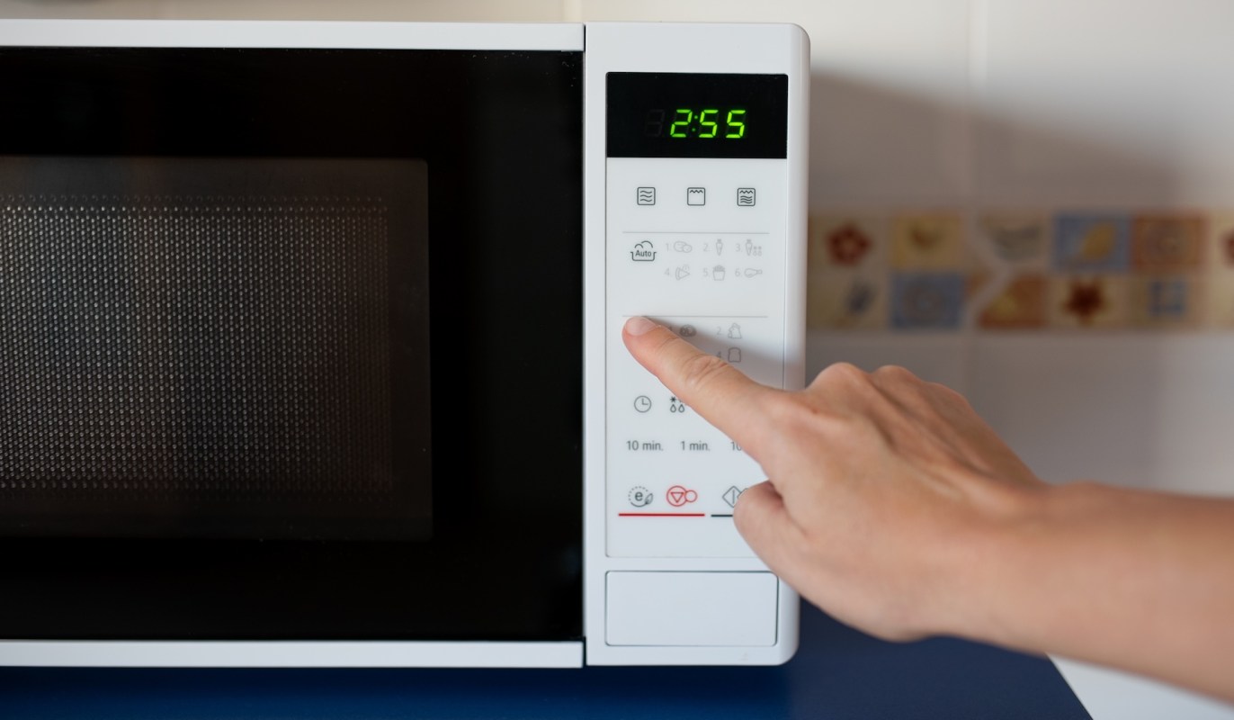 A hand pressing a button on a microwave.
